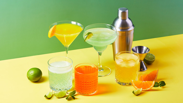 A bunch of colorful cocktails with a cocktail shaker, all against a green and yellow background