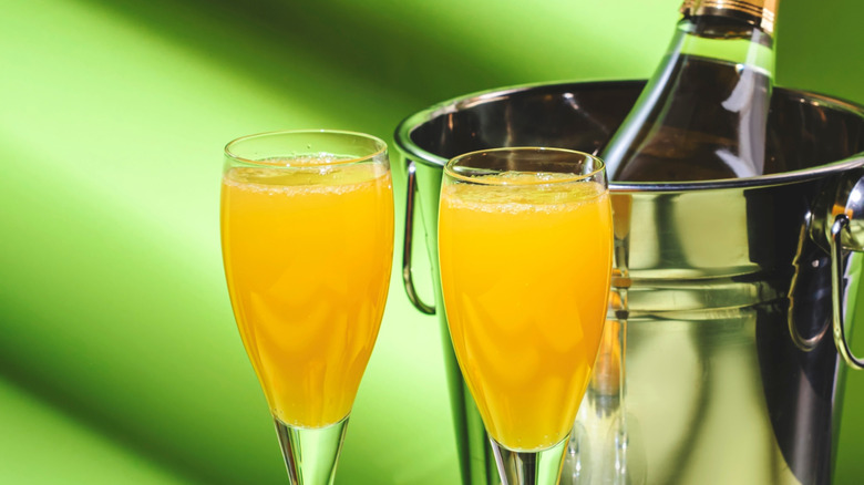 Two mango mimosa cocktails with a bottle of champagne resting in a bucket in the background