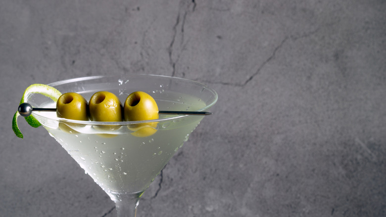 A closeup of a martini cocktail in a martini glass with three olives and a lime twist