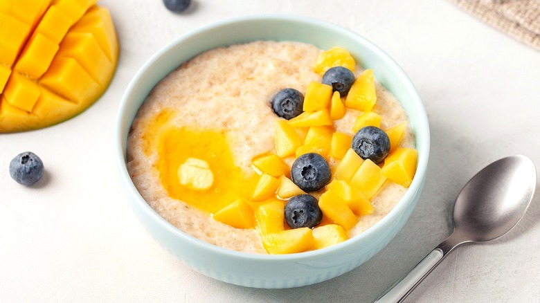 Creamy oatmeal with chopped mango and blueberries in a white bowl