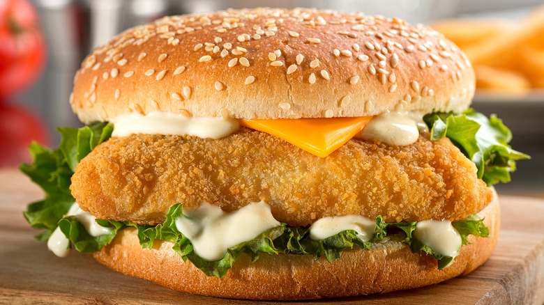 Fried fish sandwich with tartar sauce, lettuce, and American cheese on a sesame seed bun