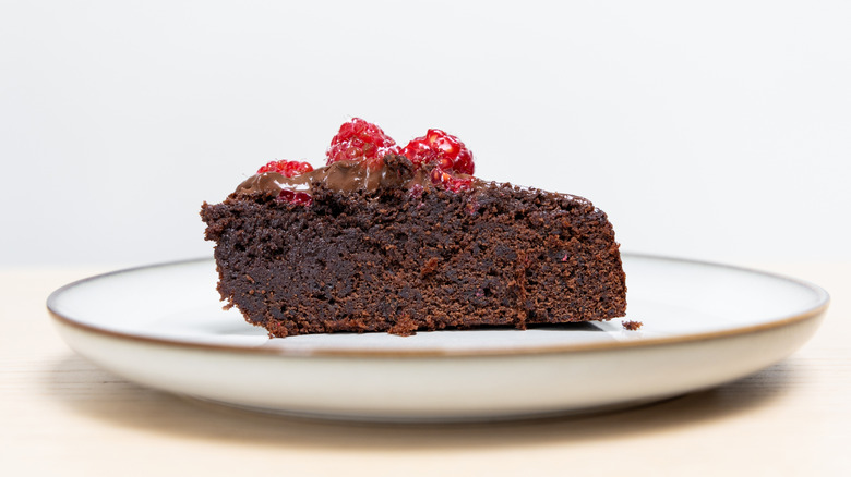Slice of chocolate mud cake with raspberries on top on a white plate