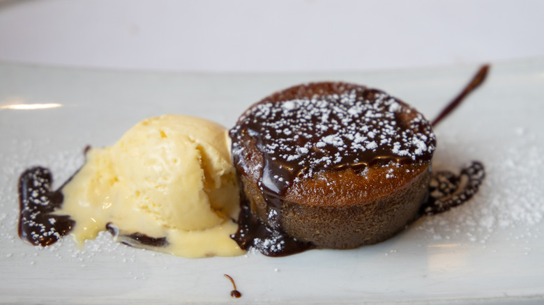 Coulant au chocolat with chocolate and powdered sugar drizzled on top, next to a scoop of ice cream