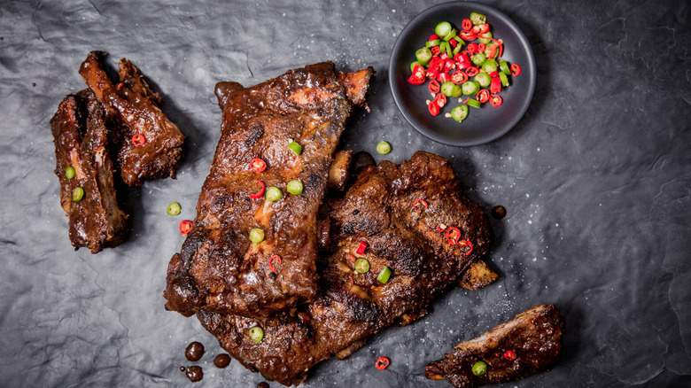 Beef ribs garnished with sliced peppers on a black slate background