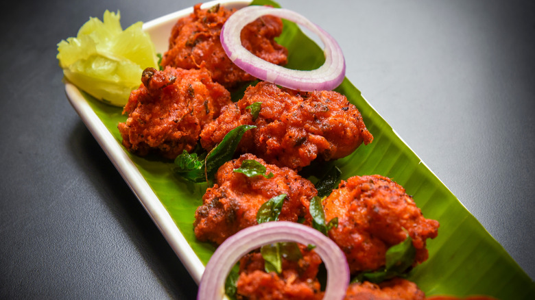 Pieces of Chicken 65 on a plate lined with a banana leaf, garnished with red onion slices