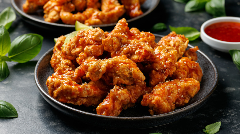 A pile of Korean fried chicken on a black plate, with another plate of chicken in the background