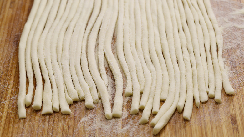 Long strands of pici freshly made on a wooden table