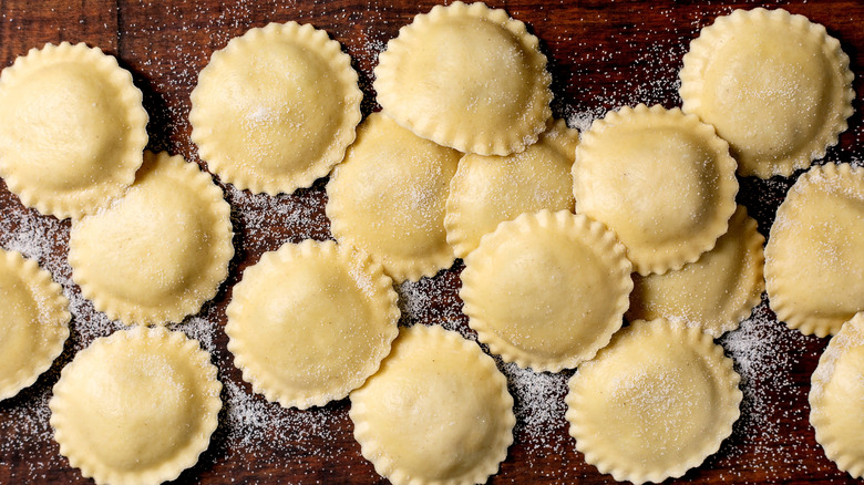 Circular ravioli sprinkled with semolina flour on a wooden cutting board
