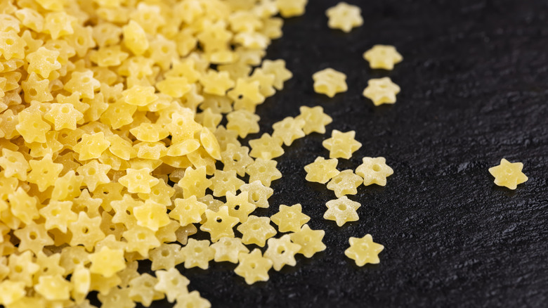 Dry stelline pasta scattered on a black surface