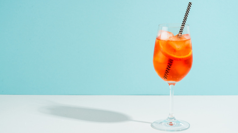 An Aperol spritz with striped straw on a light blue background.