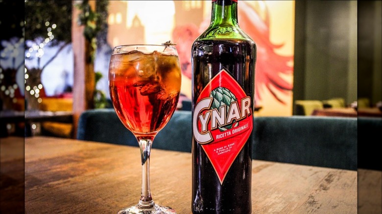 A Cynar spritz next to a bottle of Cynar.