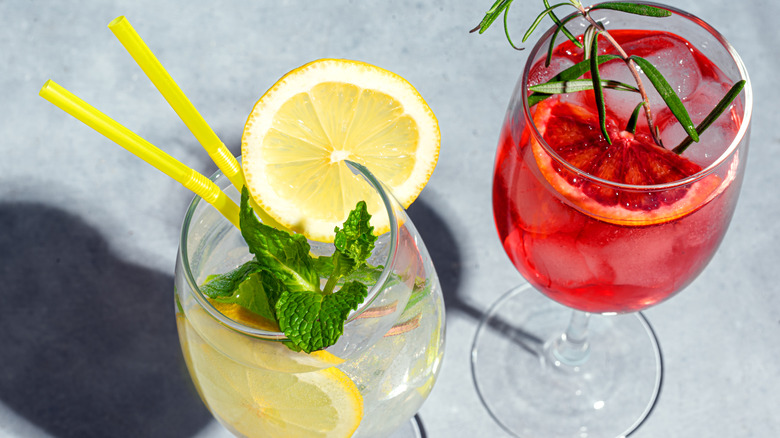 An overhead view of a Hugo and Campari spritz with herb garnishes.