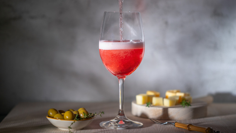 Someone pouring Lambrusco into a spritz with cheese and olives in the background