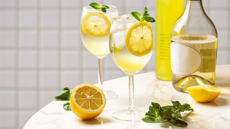 Two limoncello spritzes with various garnishes and bottles in the background