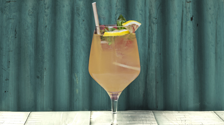 An amaro spritz in wine glass with fruit and herb garnishes.