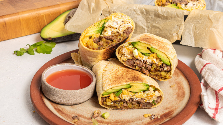 Three burrito halves on a plate with a side of red sauce