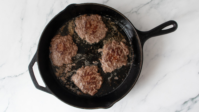 flattened burgers cooking in a skillet