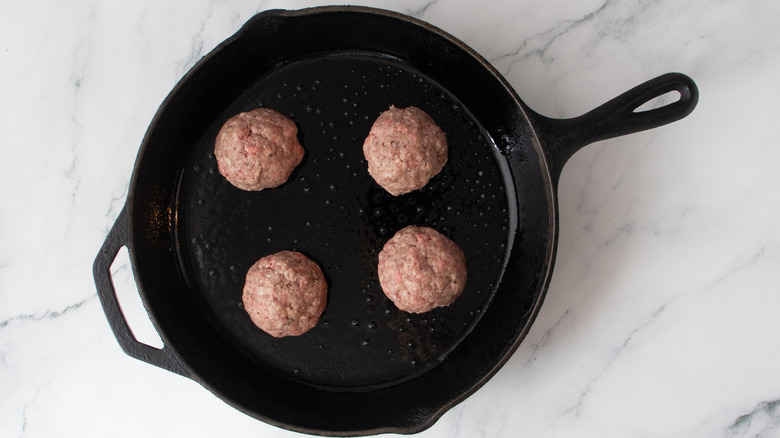 four balls of ground beef in a skillet
