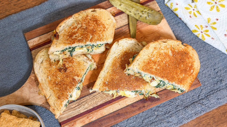 Ultimate spinach artichoke grilled cheese halves with pickles on cutting board
