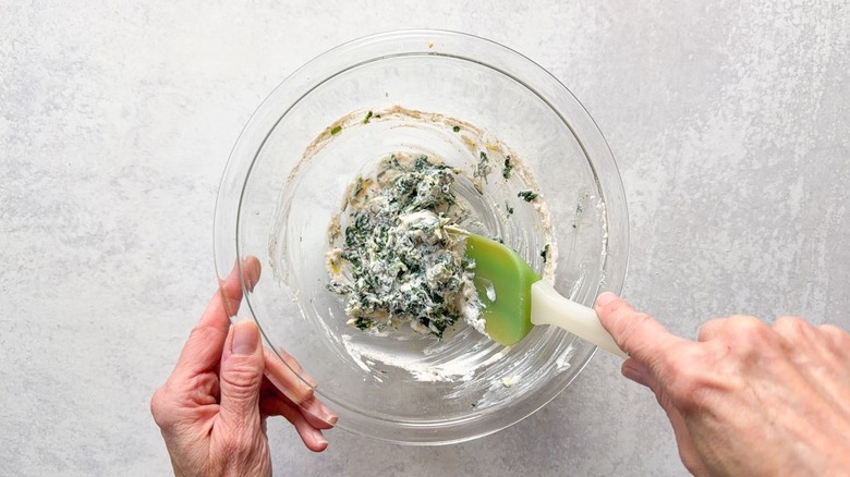 Folding chopped spinach into whipped ricotta with spatula in glass bowl