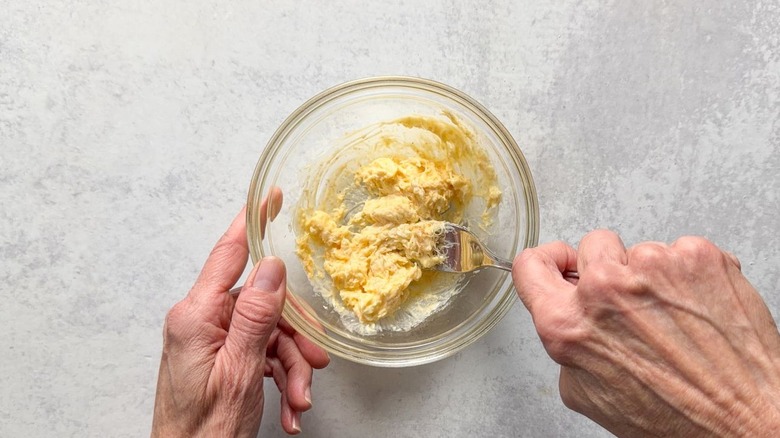 Mixing mayonnaise, butter, parmesan, and garlic powder into a paste in glass bowl