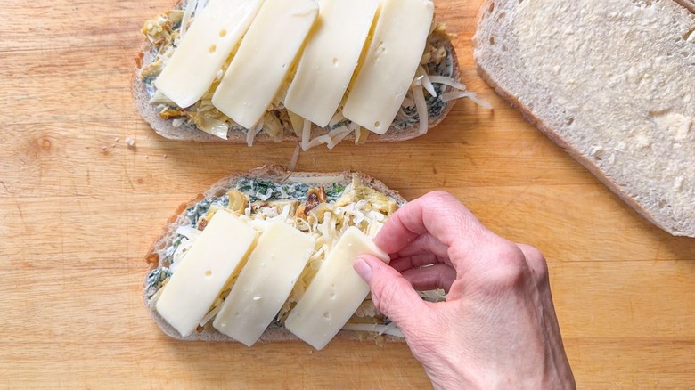 Adding sliced cheese to spinach artichoke mix on bread