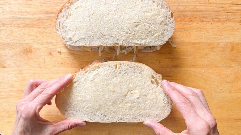Placing buttered bread atop a spinach artichoke sandwich ready to be grilled