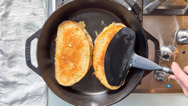 Ultimate spinach artichoke grilled cheese sandwiches in skillet on stovetop with spatula