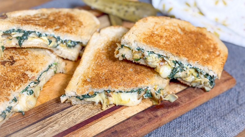 Ultimate spinach artichoke grilled cheese sandwich halves stacked on cutting board