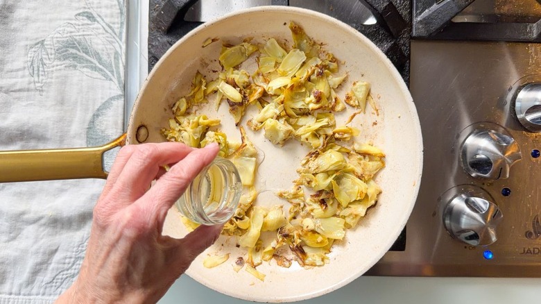 Adding wine to skillet with browned artichoke hearts and garlic