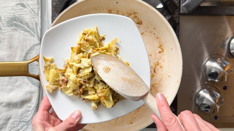 Using wooden spoon to transfer artichoke hearts from skillet to plate