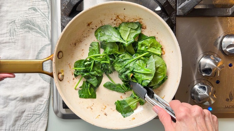 Sauteeing baby spinach in skillet with tongs