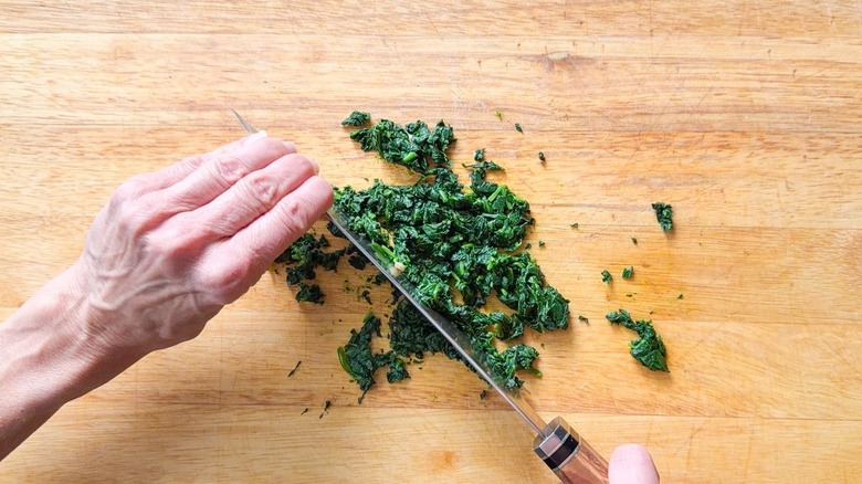 Chopping cooked spinach on wooden cutting board