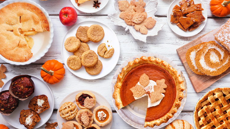 A large display of a variety of fall desserts on a white wooden table.