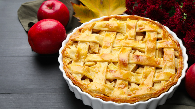A homemade pie sits next to two apples and maple leafs.