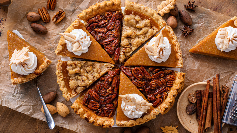 A mix of slices of pumpkin and pecan pie topped with whipped cream.