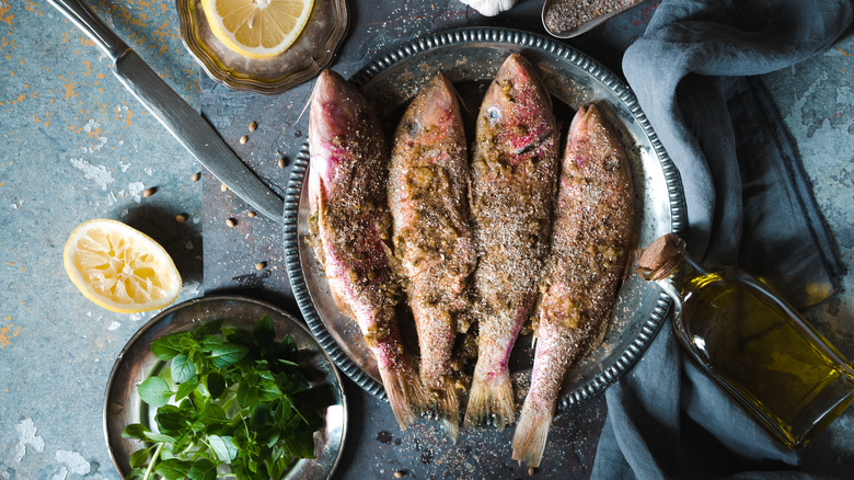 Red mullet on a dinner plate with lemon halves, olive oil, spices, and herbs