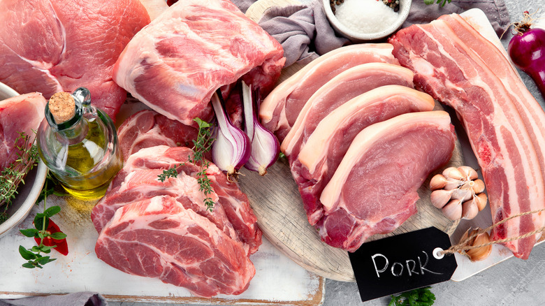 Various cuts of pork on a table with oil, garlic, onions, and herbs on the side