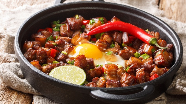 A plate of pork sisig with a chili, egg, and lime slice on top.