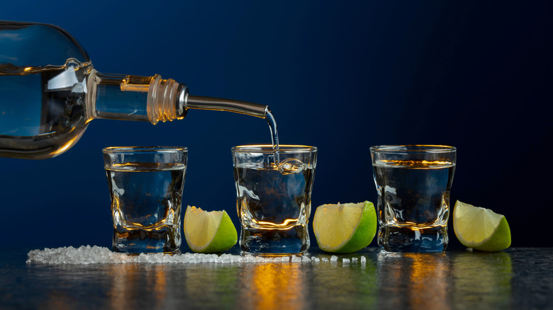Pouring tequila into three shot glasses surrounded by salt and lime wedges