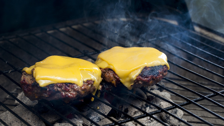 Beef patties with melted cheese are cooking on a grill.