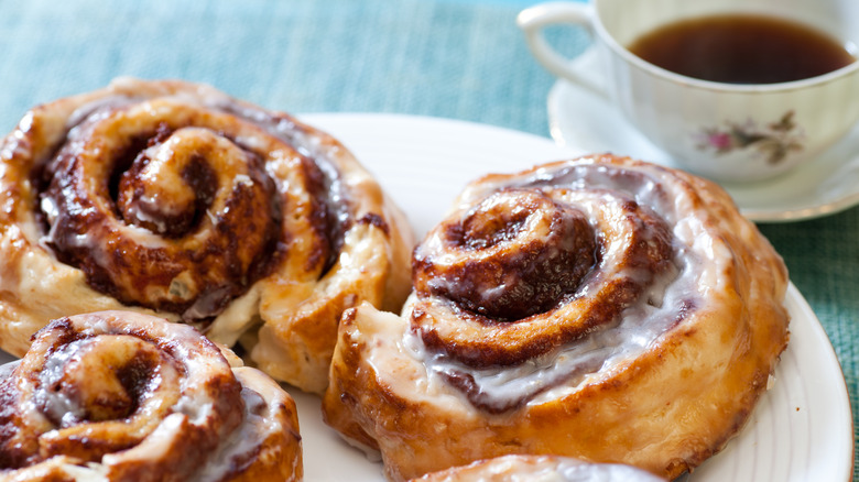 A plate of cinnamon rolls is next to a cup of coffee.