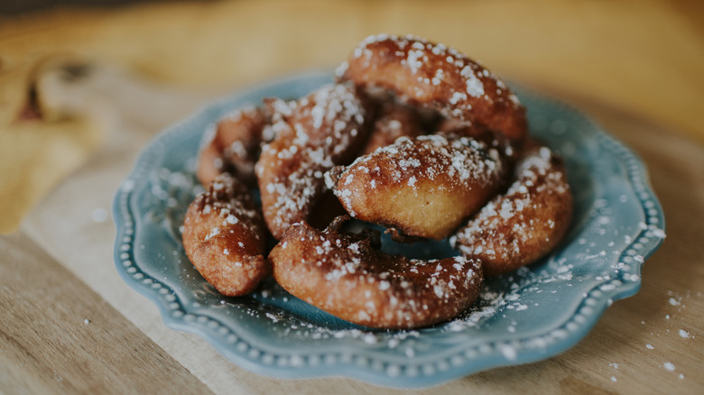 A plate of fritters is sprinkled with powdered sugar.