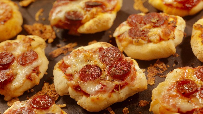 Homemade mini pepperoni pizzas are shown on a pan.