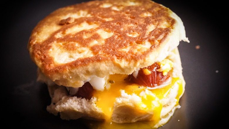 A closeup shows a breakfast biscuit filled with runny egg and sausage.