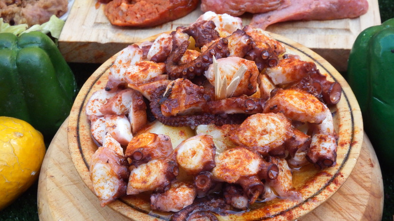 Large plate of cut and seasoned octopus with different meats and sausages on a cutting board in the background