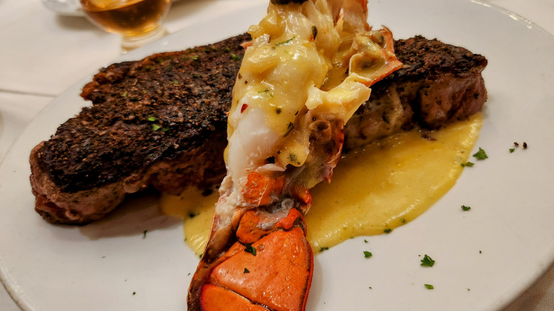 Closeup of marinated steak topped with a lobster tail on a plate