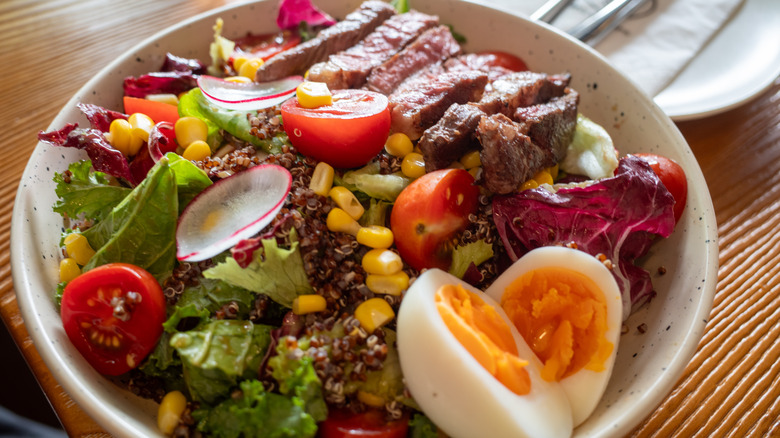 Salad with many ingredients including steak, hardboiled eggs, and likely fish somewhere