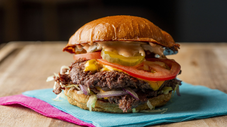 Hamburger with tomatoes, pickles, and onions on napkin