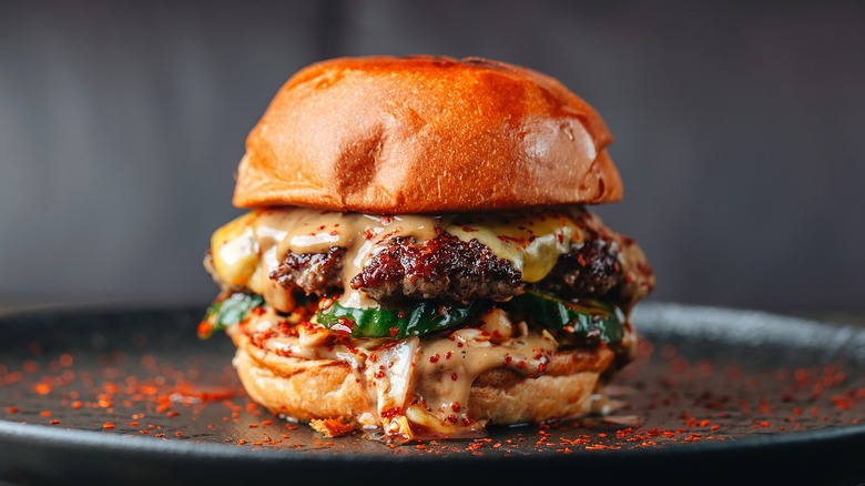 A close-up of a burger is shown with melted cheese and chili flakes on a black plate